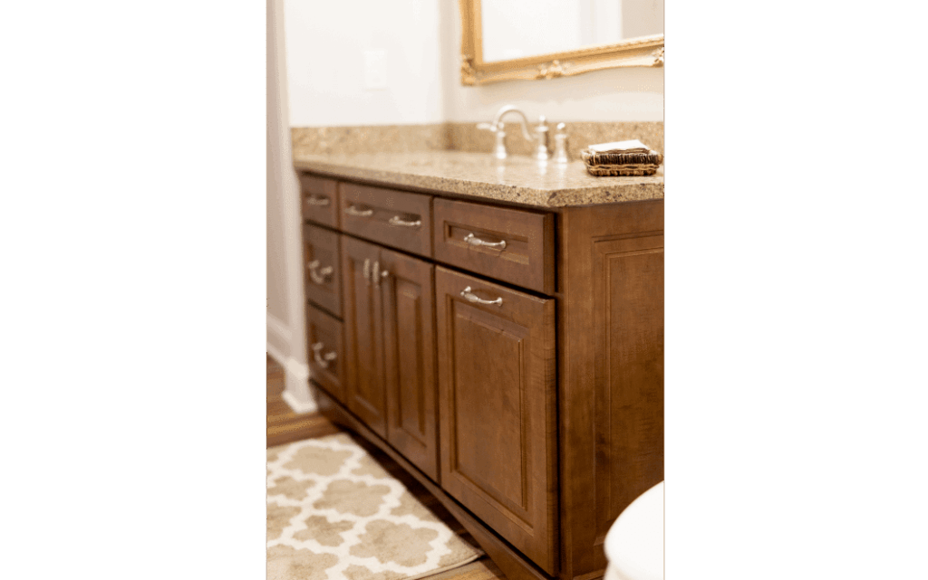 Remodeled bathroom with woodgrain sink vanity with multiple drawers and cabinets. Tan stone countertop.