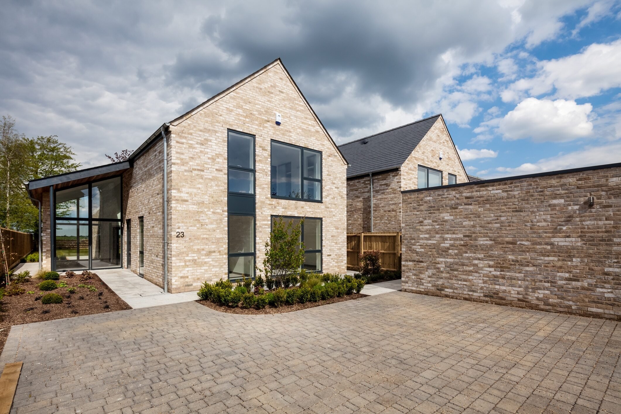 Two-story light brick contemporary style home with black-framed windows, A-frame roof, and sunroom addition on the left.
