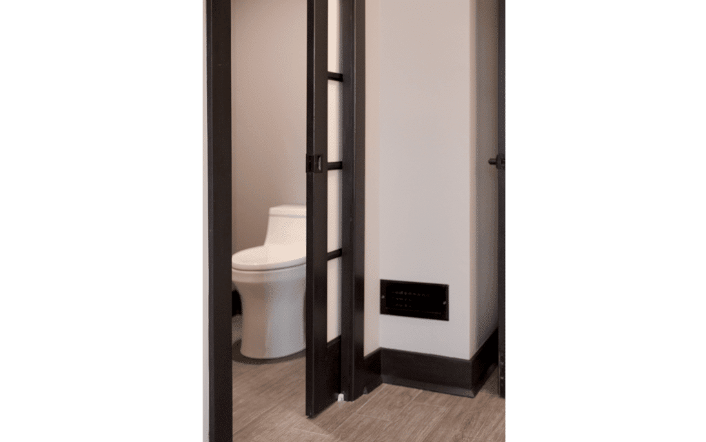 Remodeled primary suite with pocket door mostly open, leading to en-suite bathroom with wide doorway and comfort-height toilet.