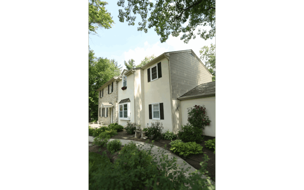 Exterior of a large colonial style home with two-story additions built onto right side. Trees surrounding.