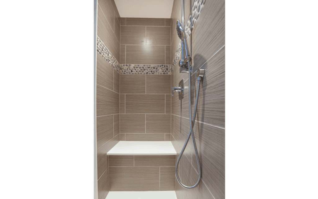 Remodeled standing shower with large tan tiles and pebble accent strip across upper half of the wall.