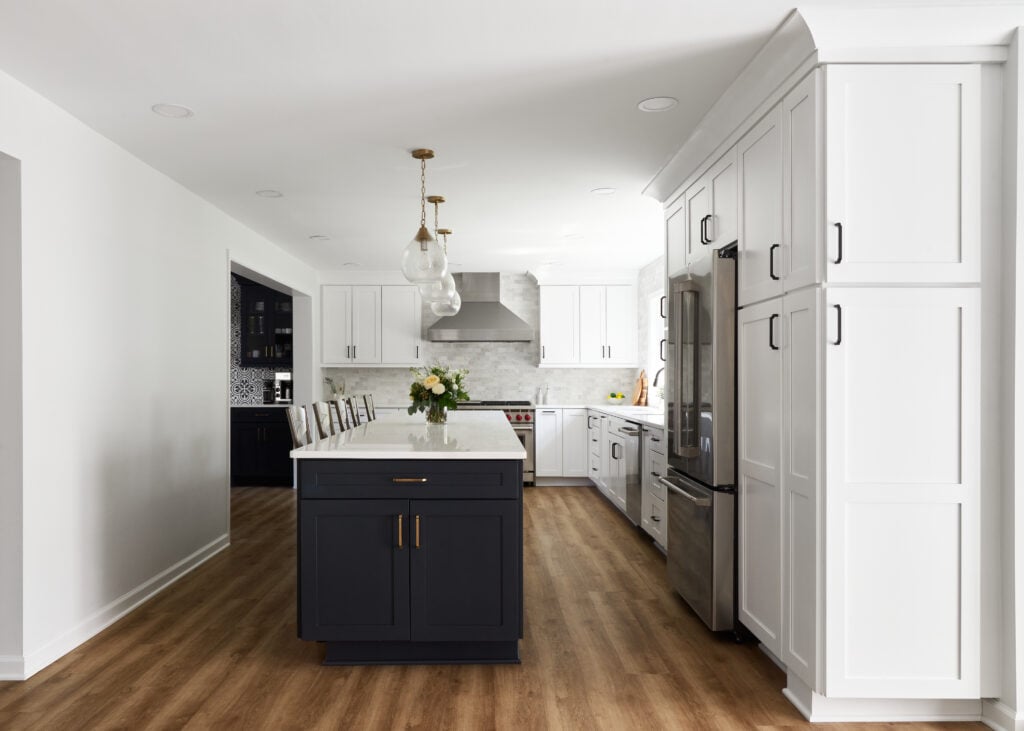 Hardwood flooring in a remodeled white kitchen with black cabinet island and white countertops and walls.