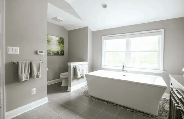 Bathroom remodel with white stand alone tub and twin double-hung windows with grids. Light gray walls and tile floor