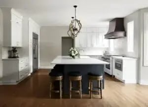 Finished product of a custom kitchen design. White kitchen with large island in middle. White stone countertops, stool seating at the island, wood floors (2) (1)