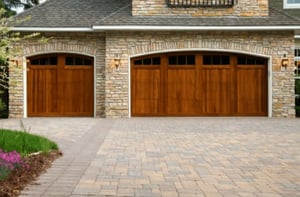 Garage addition outside view. Wood-grain garage doors with small windows in the top, on a tan brick home.