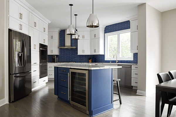 Kitchen remodel with wood floors, blue cabinet island, white cabinets along walls, blue tile backsplash.