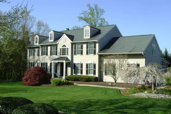 Large two-story colonial-style home with white siding, black shutters, three dormers, and large manicured front lawn. Addition on the right side.