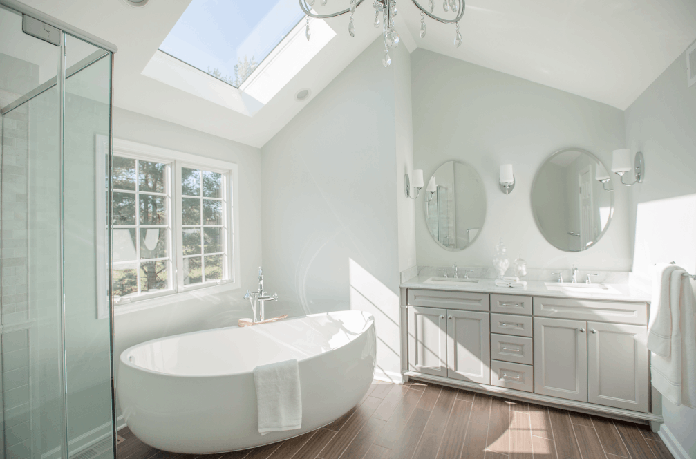 Bright airy bathroom remodel with double circle mirrors over vanity, skylight over soaking tub, glass shower.